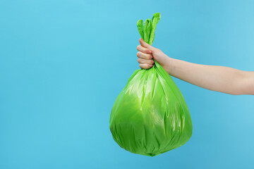 Woman holding plastic bag full of garbage on light blue background, closeup. Space for text