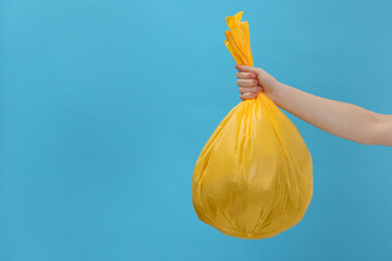 Woman holding plastic bag full of garbage on light blue background, closeup. Space for text