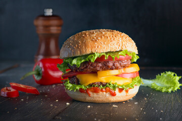 Delicious and flavorful double burger with bun, grilled meat, cheese, tomatoes on a wooden background with a place to copy
