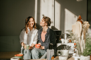 Cozy morning: girls friends talking over a cup of coffee in a bright kitchen Two women spend time...