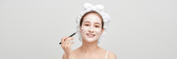 Beautiful young woman with clay facial mask, beauty treatment over white banner