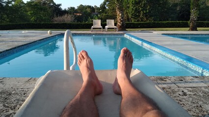 first-person point of view where you can see the legs resting on a chair with the bottom of a pool...