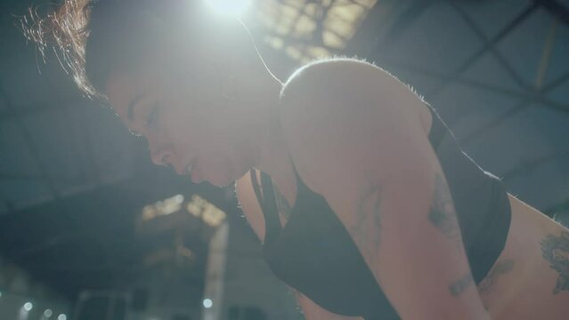 Young tired female athlete standing with hands on thighs and heavily breathing after hard workout in the gym