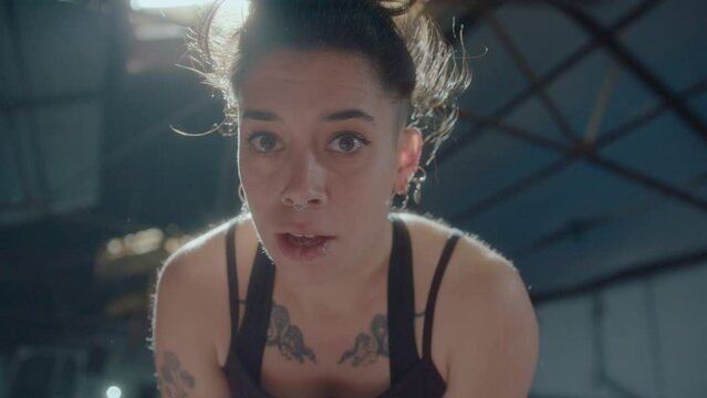 Young tired sportswoman with sweat on her face breathing heavily and looking at camera after intense workout in a gym. Zoom shot, video portrait