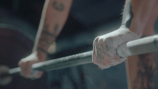Hands of unrecognizable female weightlifter gripping barbell and making clouds of chalk powder dust flying in the air in the gym. Close up shot