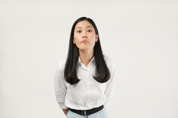 Pouting with slightly puffed cheeks, an Asian woman in white conveys displeasure and thoughtfulness in a workplace setting, showing reflective and reserved emotions