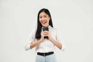 The photo of a young Asian woman holding her phone feeling excited, reads news holding modern cellular in her hands looking with a curious happy expression, isolated on a white background. 