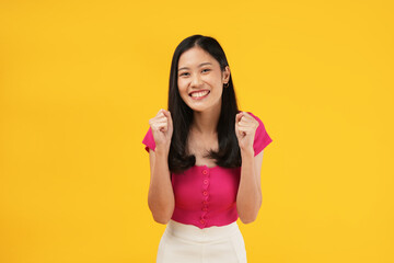 Photo of a young Asian woman excited to celebrate success, dressed a pink t-shirt and isolated on a yellow background. 