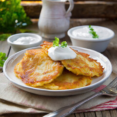 A plate of Polish placki ziemniaczane potato pancakes served with a dollop of sour cream in a rustic setting.