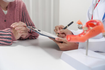 female doctor reassuring patient with comforting hand gesture, with model of the female reproductive system on table, possibly discussing menstruation, cervical cancer, infertility, or sterilization.