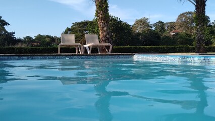 swimming pool with palm trees on a summer day, reflection of the sun in the water, point of view from inside the pool