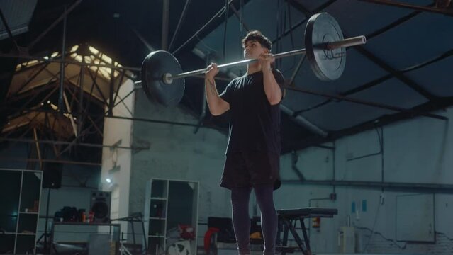 Young male athlete in sportswear doing barbell overhead press during weightlifting workout in the gym