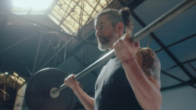 Strong middle aged man with muscular arms doing barbell bicep curls during weight training workout in a gym