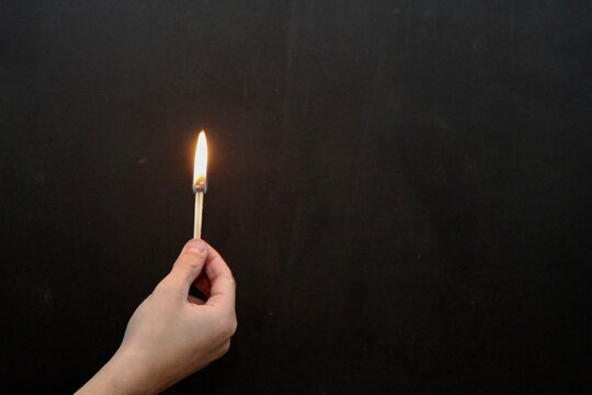 Hand holding a lit match against dark background