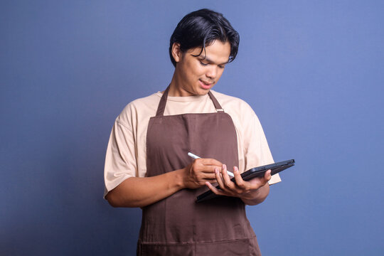 Young waiter wear apron taking order using tablet isolated over blue background