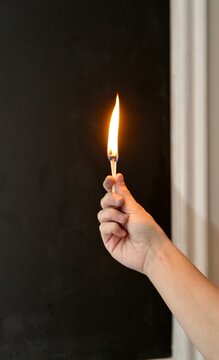 Hand holding a lit match against dark background