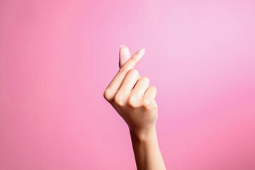 Female hand gesturing showing heart from fingers, korean love symbol over pink background