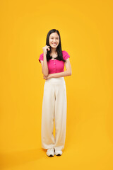 Obraz premium An Asian woman stands confidently with her hand on her hip, radiating poise and positivity against a bold yellow background