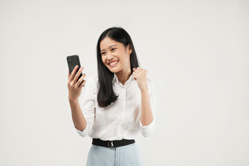 Fototapeta premium Photo of a young Asian woman smiling and celebrating good news on phone notification, dressed a white shirt and isolated on a white background. Positive message. 
