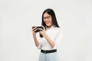 This portrait of a young Asian woman wearing a white shirt and glasses, with a positive expression playing video games on a modern smartphone, isolated on a white background. Modern technology concept