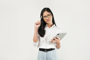 An Asian woman holds a tablet while thoughtfully tapping her pen against her chin, exuding a contemplative and focused demeanor in a professional setting.