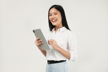 Photo of an Asian woman 20s standing and holding a tablet, dressed a white shirt and isolated on a white background. 