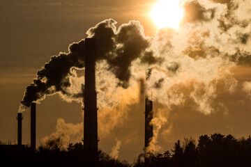 Silhouette of heavily smoking tall chimneys against the backdrop of the bright sun