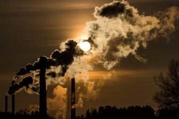 Silhouette of heavily smoking tall chimneys against the backdrop of the bright sun
