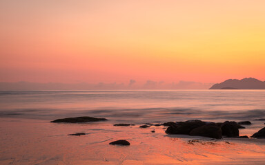 Orange sunrise glow and reflections on a tropical beach and islands at Rose Bay in Bowen in the...