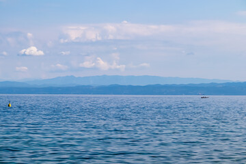 Obraz premium Panoramic view of idyllic coastline seen from Gulf of Piran, Adriatic Mediterranean Sea, Slovenia, Europe. Summer seaside vacation. Distant mountain ranges of Julian Alps. Ships floating in calm water