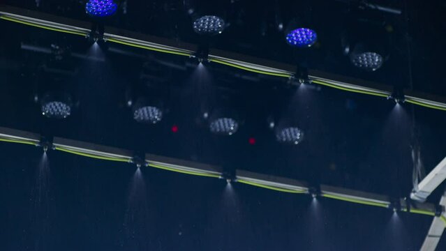 A special effects rain machine in a film cinema studio with a ceiling full of film lights. Led cinema lights strobe as water sprays from sprinklers on the device.