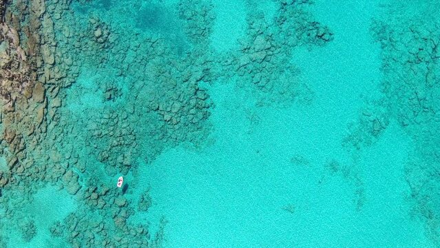 Drone view in Greece top view ocean clear blue water with rocks on the bottom a small white boat on a sunny day