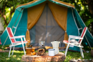 selective focus of vintage coffee set on the old wooden table In front of the retro cabin tent, retro chairs, Group of camping tents, and soft focus.