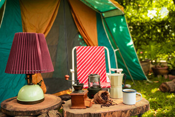 selective focus of vintage coffee set on the old wooden table In front of the retro cabin tent, Antique oil lamp, retro chairs, Group of camping tents, and soft focus.