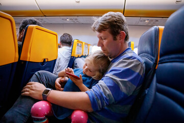Young father holding his baby toddler daughter during flight on airplane going on vacations. Tired...
