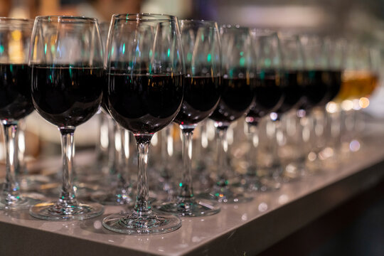 Wine glasses filled with red wine arranged and presented on a table top for self-service by party guests. Shallow depth-of-field image. A glass of red wine is on the table. Glasses of wine.

