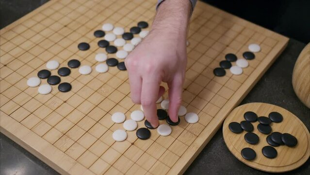45 degree overhead angle of hand playing white stone in Go board game with tiles already on grid and black pieces in corner