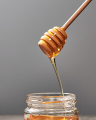 Dripping meadow organic natural honey from wooden dipper into a pot on a gray backgroun, pure raw...