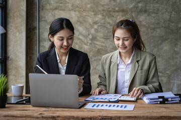 Two Asian female accountants have team meeting to summarize financial information in business...