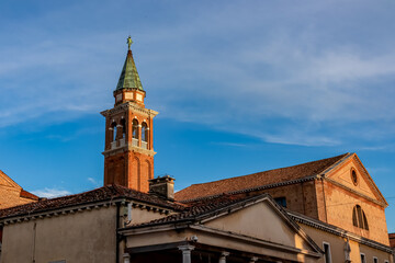 Fototapeta na wymiar Close up view at sunrise of bell tower of Church of Saint James Apostle nestled in charming town of Chioggia, Venetian Lagoon, Veneto, Italy. Sightseeing in historic old town of Chioggia. Sightseeing