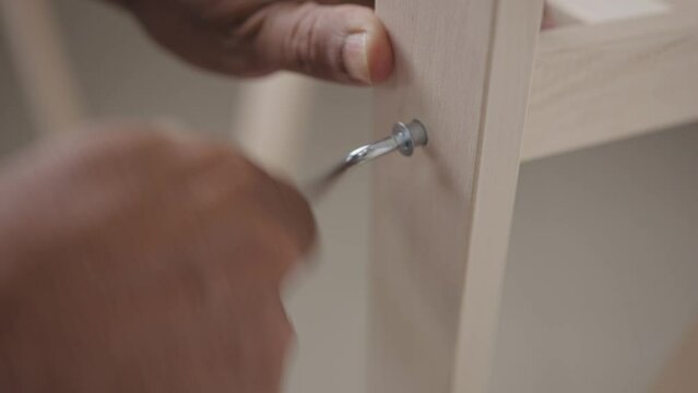 Close-up of the hand of a man going to tighten a nut with a tool. There is a wooden piece of furniture in the picture.