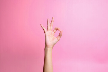 Hand showing ok sign with fingers isolated over pink background. Hand gesture