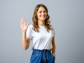 Portrait of friendly woman waiving hand to say hi, greeting you with hello gesture - obrazy, fototapety, plakaty