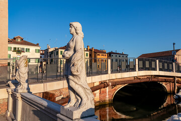 Collection of ancient statues graces peaceful water canal in the charming town of Chioggia,...