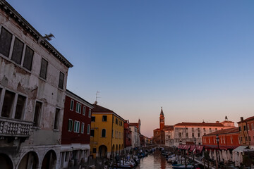 Church of Saint James Apostle with sunset view of canal Vena nestled in charming town of Chioggia, Venetian Lagoon, Veneto, Italy. Small boats floating in calm water creating romantic reflections