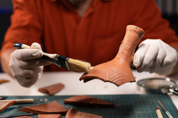 Male archaeologist dig ancient pottery object working in archaeological office at night. - obrazy, fototapety, plakaty