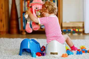 Closeup of cute little 12 months old toddler baby girl child sitting on potty. Kid playing with...