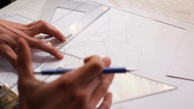 Closeup view of experienced architect drawing blueprints, planning a building. Close-up of blueprint paper on the table. Architect checking building drawing, design bureau, hands closeup.