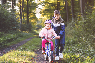 Cute little preschool girl in safety helmet riding bicycle. School kid boy, brother teaching happy...