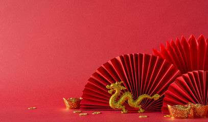 Festive Lunar New Year setting: side view table adorned with feng shui essentials, gold coins, dragon figurine, and fans on a vibrant red backdrop. Empty space for text - obrazy, fototapety, plakaty